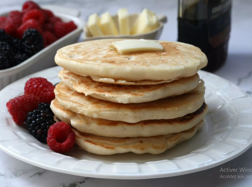 Stack of golden pancakes with maple syrup and berries.