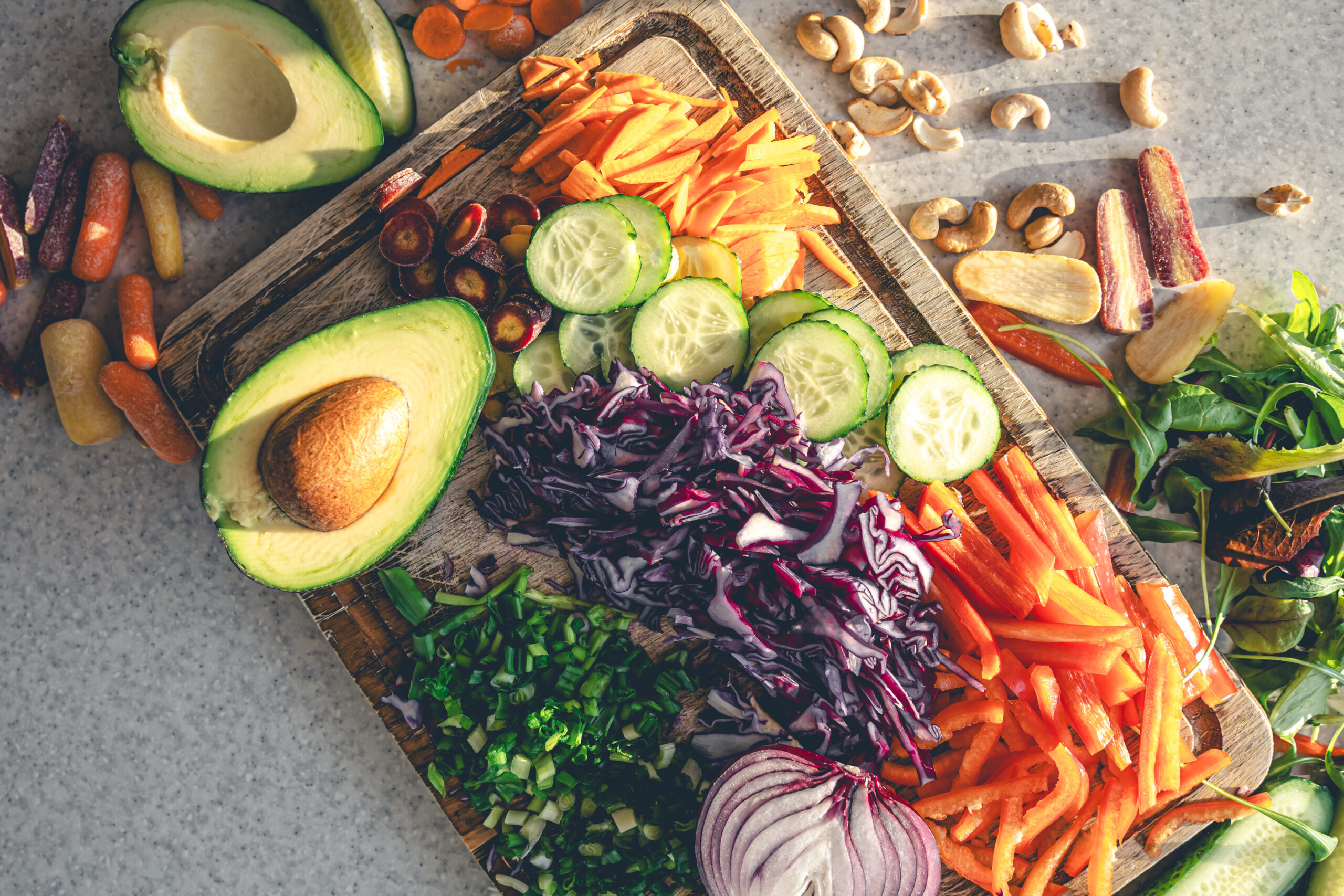 Freshly sliced vegetables including avocado, cucumbers, red cabbage, and carrots on a cutting board – perfect ingredients for raw and vegan recipes.