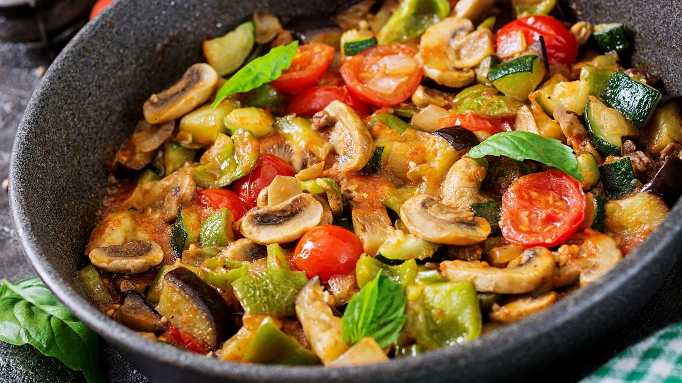 Colorful vegetable casserole with zucchini, mushrooms, cherry tomatoes, and fresh basil in a skillet.