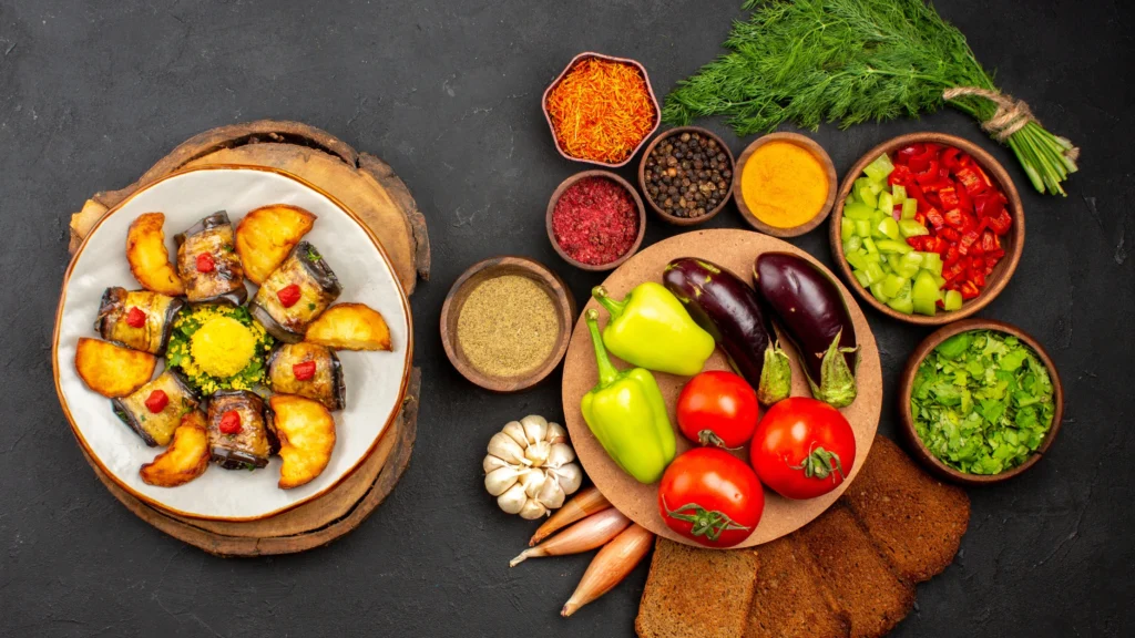 Brunch plate featuring stuffed eggplant rolls, roasted potatoes, and vibrant fresh vegetables like tomatoes and bell peppers, showcasing what a vegan eats for brunch with herbs and spices for a flavorful plant-based meal.