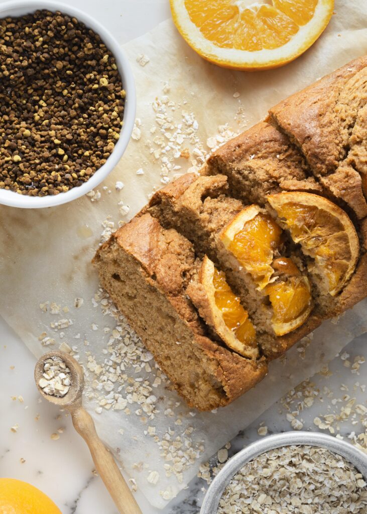 A freshly baked vegan orange loaf cake garnished with orange slices, surrounded by oats and other plant-based ingredients.