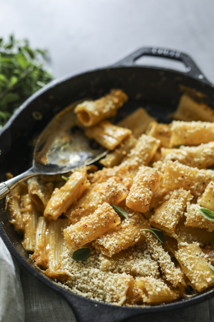 Creamy vegan roasted cauliflower Alfredo pasta baked with a golden breadcrumb crust, served in a black skillet and garnished with fresh herbs.