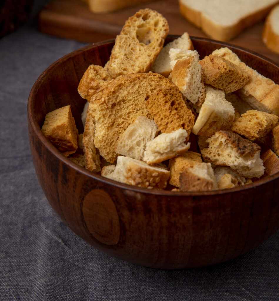 Golden-brown vegan croutons on a baking tray garnished with fresh herbs, surrounded by a bowl of salad and rustic kitchen towel.